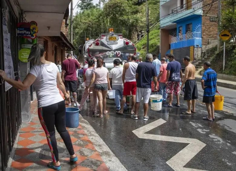 Personas con baldes y recipientes alrededor de un carrotanque de EPM en una calle tras cortes de agua en Medellín.