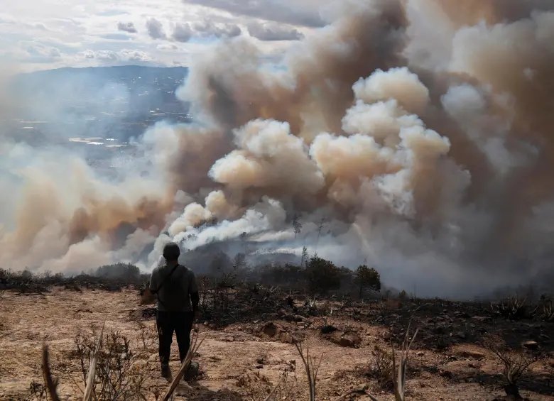 Una persona de espaldas observa una ladera cubierta por densas columnas de humo del incendio en Villa de Leyva.