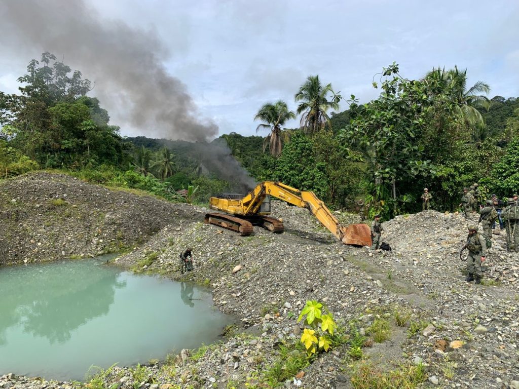 Excavadora junto a una zona intervenida y uniformados en terreno. Referencia a minería ilegal en El Bagre.