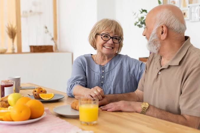 Dos personas mayores conversan mientras desayunan. Referencia a mesada pensional.