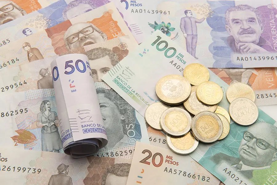 Billetes colombianos de diferentes denominaciones junto a varias monedas. Referencia a Colombia y el FMI.