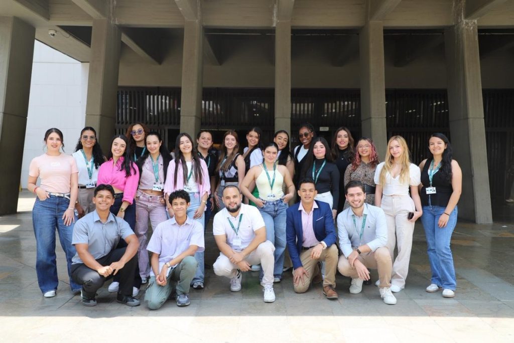 Grupo de jóvenes de Prácticas de Excelencia con carnés posa frente a un edificio institucional.