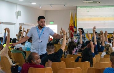 Asistentes levantan la mano durante un encuentro de participación ciudadana en un auditorio. Referencia a presupuesto participativo en Girardota