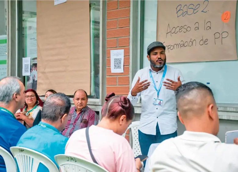 Un facilitador conversa con asistentes frente a un cartel sobre acceso a información de presupuesto participativo en Girardota.