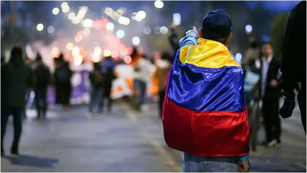 Persona de espaldas con una bandera de Colombia sobre los hombros durante protesta social.