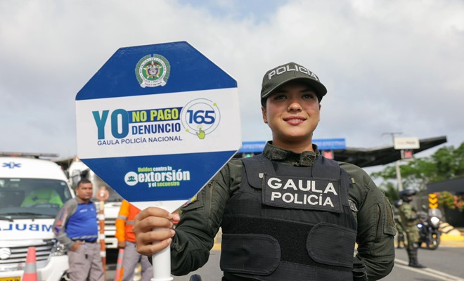 Integrante de la Policía sostiene un aviso de la campaña Yo no pago, yo denuncio. Referencia a panfletos falsos.