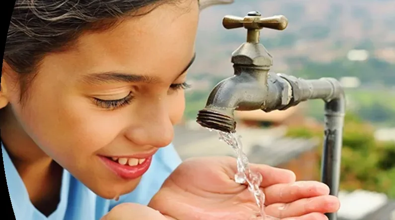 Niña recoge agua de un grifo con las manos. Referencia a cortes de agua en Medellin.