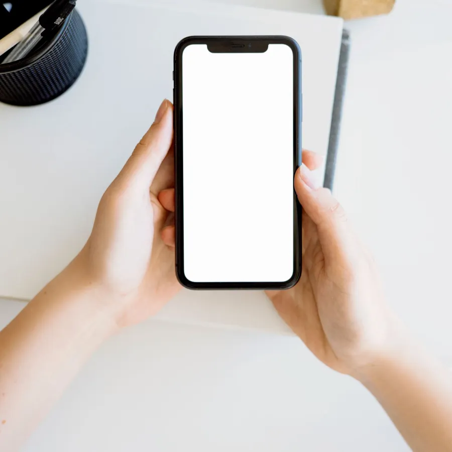 Manos sostienen un teléfono móvil con la pantalla en blanco.