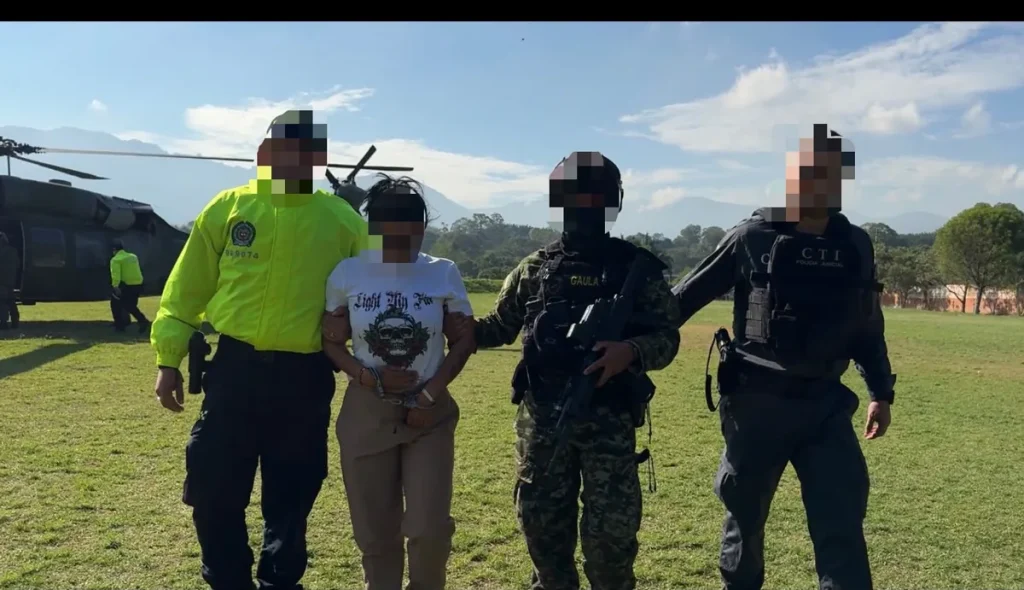 Alias Samanta, capturada junto a Alias Lobo, custodiada por integrantes de la Policía, el Ejército y el CTI, con un helicóptero al fondo.