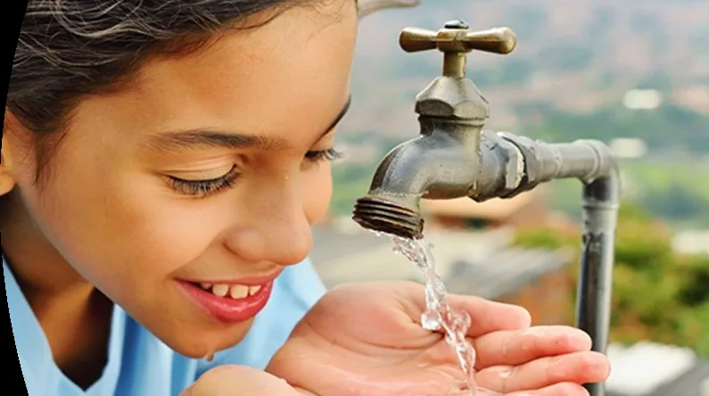 Niña recoge agua de un grifo con las manos. Referencia a corte de agua.