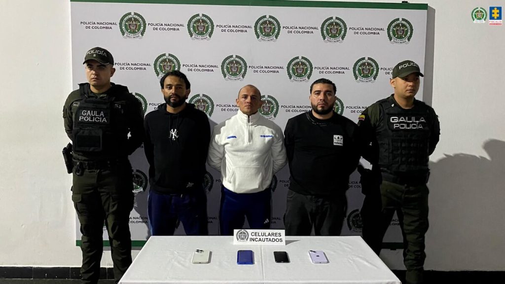 Tres hombres de La Terraza custodiados por dos agentes del Gaula detrás de una mesa con cuatro celulares incautados.