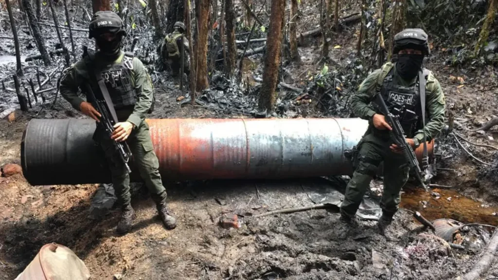 Dos uniformados armados junto a una estructura metálica cilíndrica en una zona boscosa. Referencia a Fuerza de Tarea Urano.