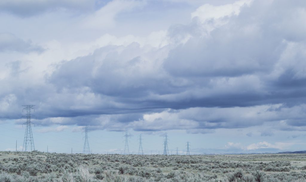 Torres y líneas de transmisión eléctrica en un paisaje rural bajo un cielo nublado.