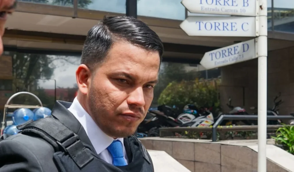 Sneyder Pinilla con camisa blanca, corbata azul y chaleco de protección en el exterior de un edificio.